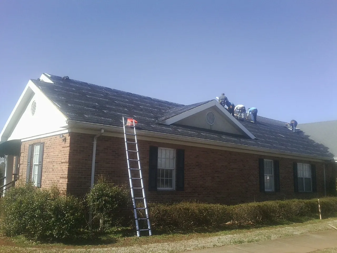 Crew tearing shingles off a brick ranch roof with a ladder set — Emergency Roof Repair work by our crew in Leicester