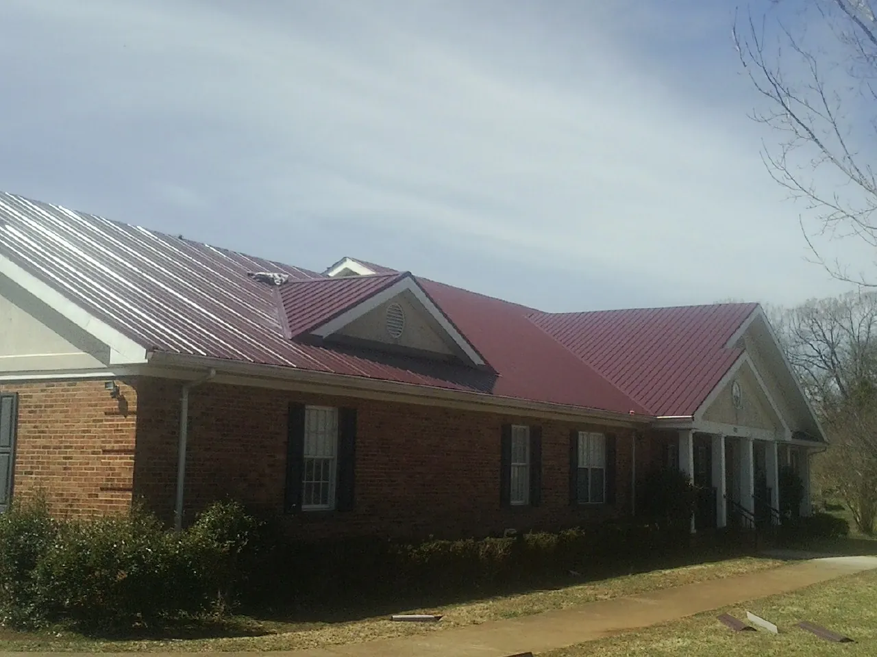 Red metal roof with gabled entries on a long brick building, from a Hail Damage Roof Repair job in Leicester