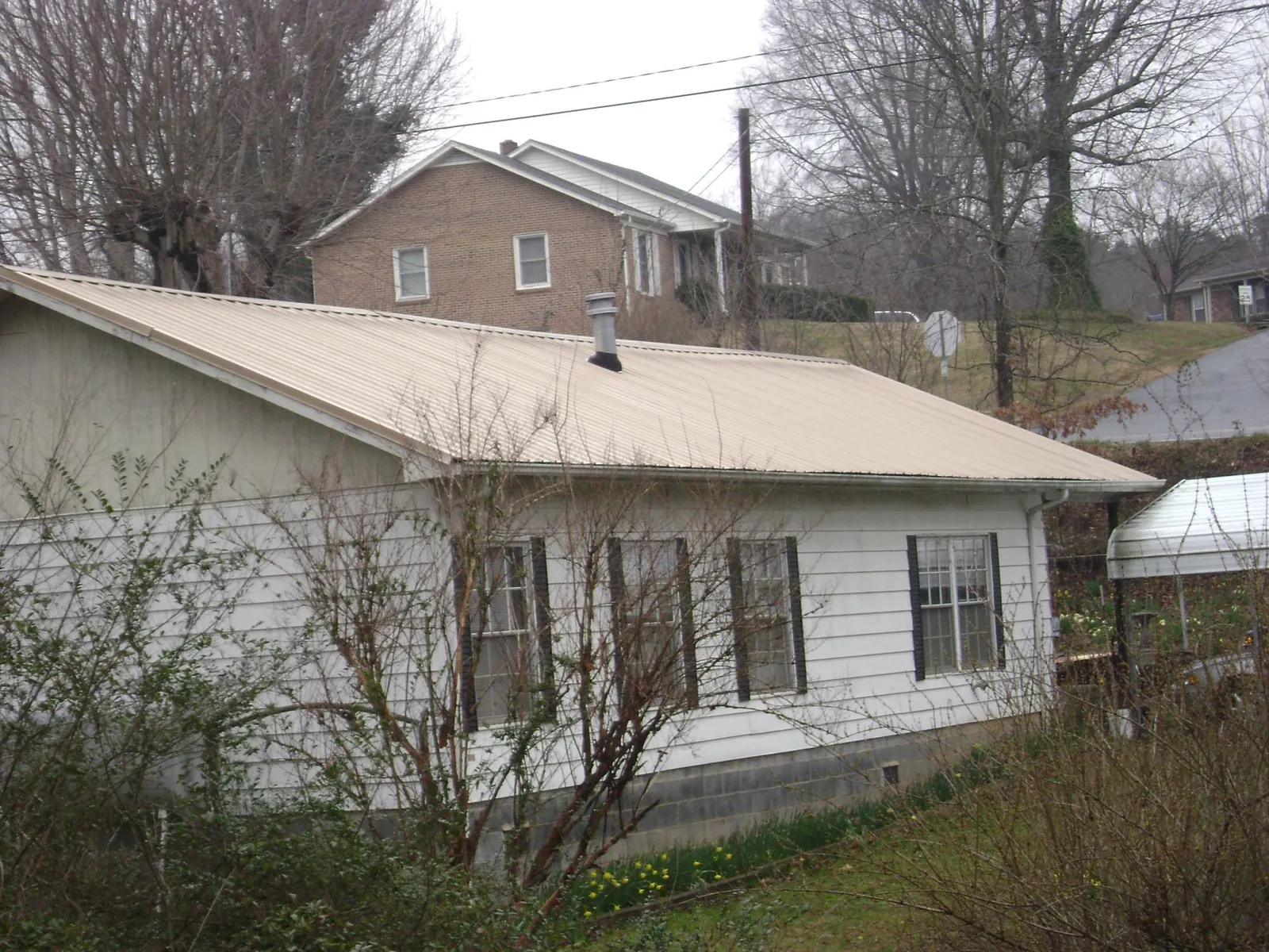 Tan metal roof on a white sided house set into a hillside — Commercial Roofing by Roofing Brothers in Leicester